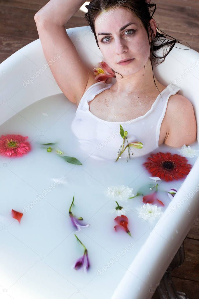 photo beautiful girl in a white T-shirt takes a natural milk bath with foam and flowers