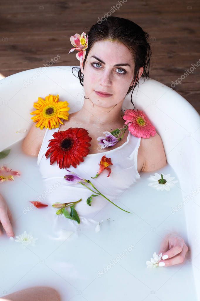 photo beautiful girl in a white dress takes a natural milk bath with foam and flowers