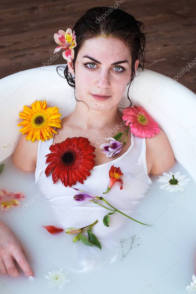 photo beautiful girl in white clothes takes a natural fragrant milk bath with foam and flowers