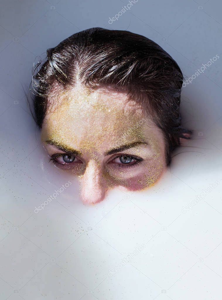 photo portrait girl in gold glitter emerges from the milk bath