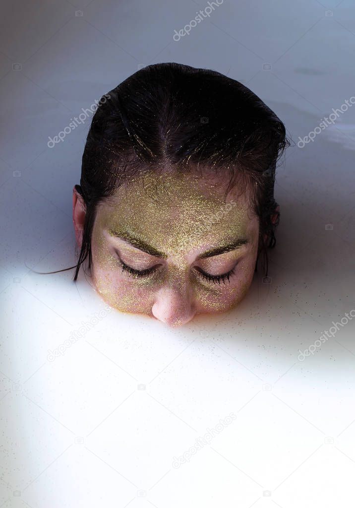photo portrait of a girl in gold glitter immersed in a milk bath