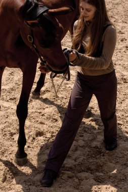 Gururlu bir kız, kumda at eğitiyor.