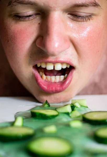 close-up of a man with an open mouth next to sliced pieces of cucumbers lying on a white table with green gel photo portrait