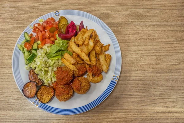 Baharatlı domates soslu ve tabakta sebzeli ev yapımı falafel. Salatalık, domates, marul, lahana, turşu, patlıcan turşusu, kızarmış patlıcan ve patates kızartması. Boşluğu kopyala