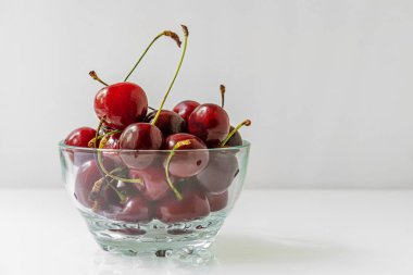 Aydınlık bir yüzeyde cam bir kasede fotokopi alanı olan tatlı kirazlar.