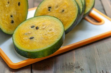 Plastik bir kesme tahtasının üzerinde sarı karpuz dilimleri