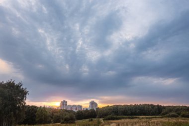 Çayır, orman ve gün batımında uzaktaki büyük şehir evleri.