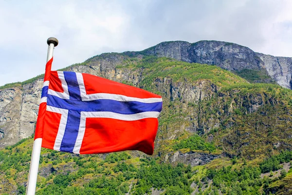 Norveç 'in ulusal bayrağı dalgalı rüzgarda ve bulutlu mavi gökyüzünde.