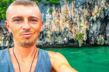 Yakışıklı erkek turist Krasom Takua Thung Phang Nga Tayland 'da kireçtaşı kayalıklarla, dağlarla, panorama deniz manzarası ve turkuaz yeşil suyla fotoğraf çekiyor..