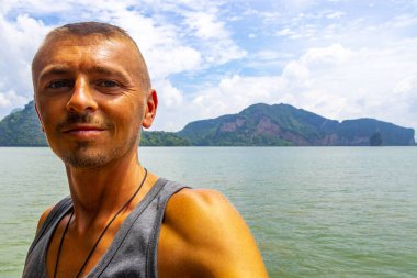 Yakışıklı erkek turist Krasom Takua Thung Phang Nga Tayland 'da kireçtaşı kayalıklarla, dağlarla, panorama deniz manzarası ve turkuaz yeşil suyla fotoğraf çekiyor..