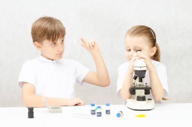Çocuklar biyoloji ve mikroorganizma okuyor. Bir kız mikroskoptan bakar, küçük bir oğlan biyolojik örneklere bakar..