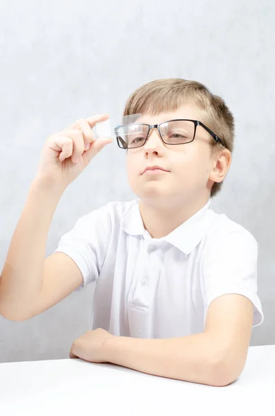 A blond-haired boy in black glasses looks at the glass with a biological sample. — ストック写真