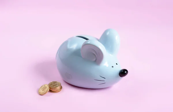 blue piggy bank in the form of a mouse with coins on a pink background