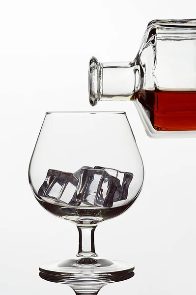 Transparent glass glass with ice cubes and a bottle of whiskey or cognac or brandy on a white isolated background