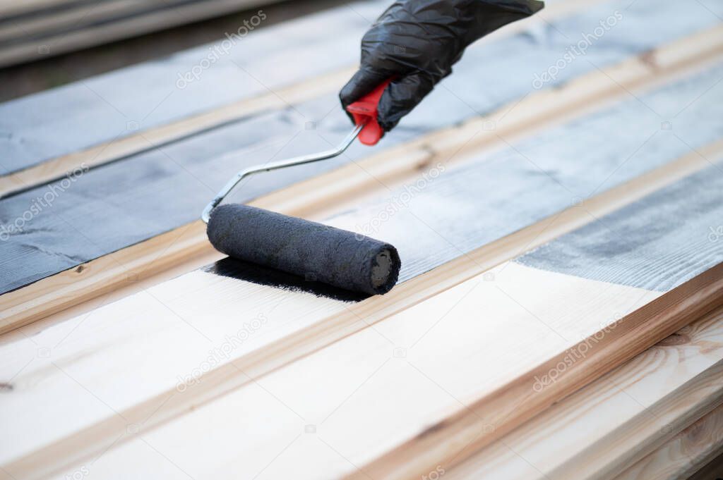 A man or woman wearing protective gloves uses a roller to paint the Board black.