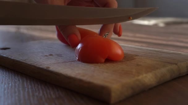 Dívka s červenou manikúrou doma, krájí červené šťavnaté rajče na kousky velký kovový nůž