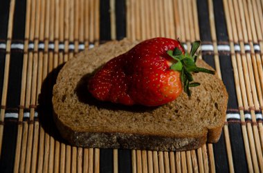 Masadaki bir parça siyah ekmeğin üzerinde çilek.