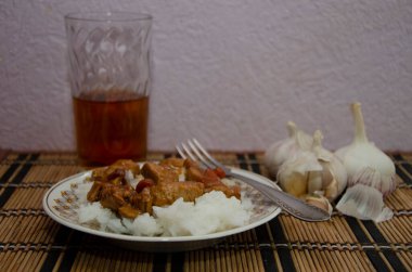 Bir tabakta çatalla sarımsak, cam, pirinç ve hindi güveci.