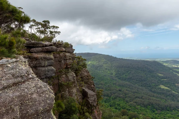 岩の多い灰色の崖の端で 木々や植生があり オーストラリアのニュースのDrawing Room Rocksで部分的に曇りの日に密なオーストラリアの森を見下ろす — ストック写真