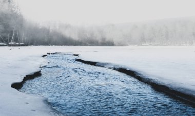 Beautiful shot of misty lake in north with ice on the side. Small foggy lake in winter time with crystal blue flowing watter. Amazing frozen and snow covered lake in Europe
