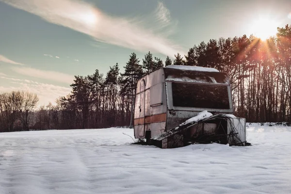 Güzel fotoğraf eski ve terk edilmiş karavan kar ortasında kış döneminde çayır kaplı. Işıklı kervan (kamp aracına) - gün batımında sezon dışı.