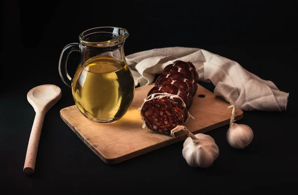 photo of salami, garlic, oil and wooden board on black background. Traditional Slovak cuisine on dark background with decor.