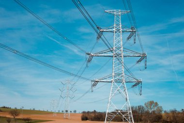 Elektrik Trafo yeni kutup, devlet ve yüksek gerilim güç hattı silueti ile mavi bulutlu gökyüzü gün batımı. Bir çok kablo ile İlkbahar alanında ışıklı iletim kulesi görünümü.