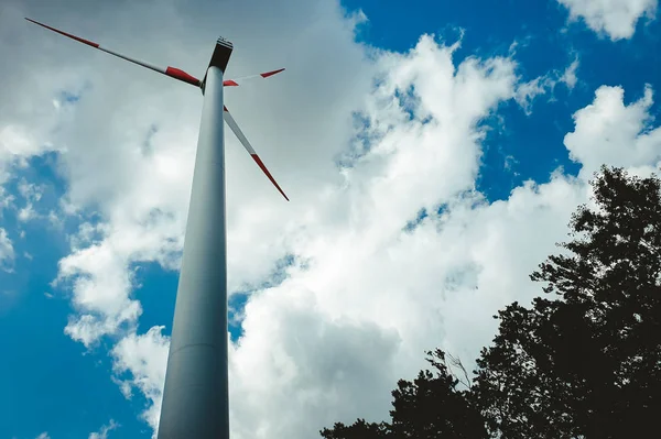 Avrupa 'daki rüzgar santrali, yerden çekilmiş bir fotoğraf. Türbin yeşil enerji elektrik teknolojisi konsepti. Yenilenebilir rüzgar enerjisi. Mavi gökyüzünde ağaç ve bulutlarla güç üreten türbin..