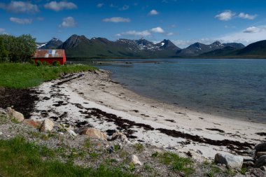Norveç 'te Lofoten' deki fiyortta Kırmızı Kulübesi ve Karlı Dağları olan Beyaz Kum Plajı