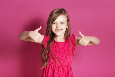 Küçük 8 yaşında kız elleri pembe tarafsız arka plan üzerinde bazı duygusal jest yapmak. O uzun esmer saç ve giyim kırmızı yazlık elbise vardır. Yüzünde komik ifade