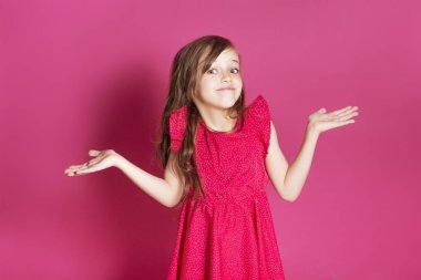 Küçük 8 yaşında kız elleri pembe tarafsız arka plan üzerinde bazı duygusal jest yapmak. O uzun esmer saç ve giyim kırmızı yazlık elbise vardır. Yüzünde komik ifade