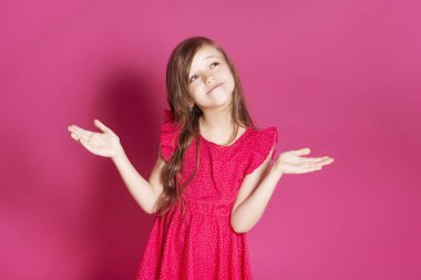 Küçük 8 yaşında kız elleri pembe tarafsız arka plan üzerinde bazı duygusal jest yapmak. O uzun esmer saç ve giyim kırmızı yazlık elbise vardır. Yüzünde komik ifade