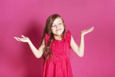 Küçük 8 yaşında kız elleri pembe tarafsız arka plan üzerinde bazı duygusal jest yapmak. O uzun esmer saç ve giyim kırmızı yazlık elbise vardır. Yüzünde komik ifade