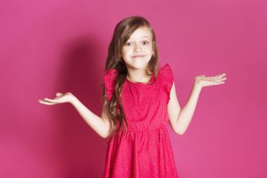 Küçük 8 yaşında kız elleri pembe tarafsız arka plan üzerinde bazı duygusal jest yapmak. O uzun esmer saç ve giyim kırmızı yazlık elbise vardır. Yüzünde komik ifade