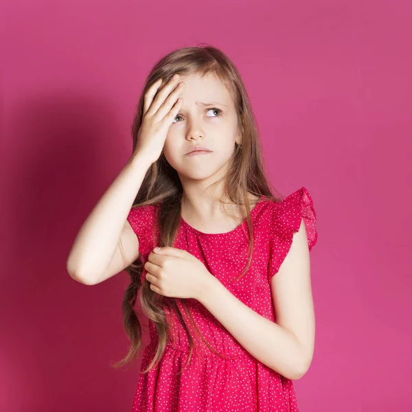 Küçük 8 yaşında kız elleri pembe tarafsız arka plan üzerinde bazı duygusal jest yapmak. O uzun esmer saç ve giyim kırmızı yazlık elbise vardır. Yüzünde komik ifade