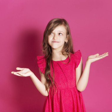 Küçük 8 yaşında kız elleri pembe tarafsız arka plan üzerinde bazı duygusal jest yapmak. O uzun esmer saç ve giyim kırmızı yazlık elbise vardır. Yüzünde komik ifade