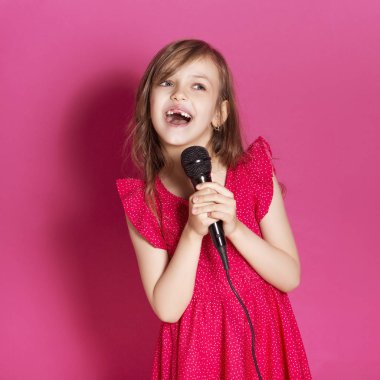 Küçük 8 yaşında kız elleri pembe tarafsız arka plan üzerinde bazı duygusal jest yapmak. O uzun esmer saç ve giyim kırmızı yazlık elbise vardır. Yüzünde komik ifade