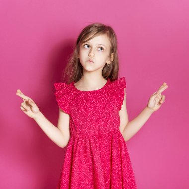 Küçük 8 yaşında kız elleri pembe tarafsız arka plan üzerinde bazı duygusal jest yapmak. O uzun esmer saç ve giyim kırmızı yazlık elbise vardır. Yüzünde komik ifade