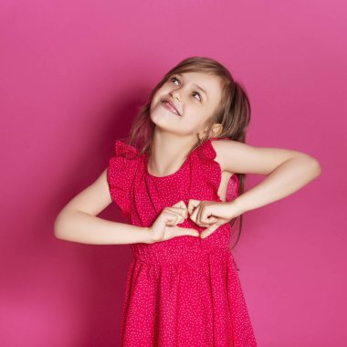 Küçük 8 yaşında kız elleri pembe tarafsız arka plan üzerinde bazı duygusal jest yapmak. O uzun esmer saç ve giyim kırmızı yazlık elbise vardır. Yüzünde komik ifade