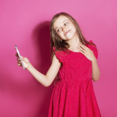 Küçük 8 yaşında kız elleri pembe tarafsız arka plan üzerinde bazı duygusal jest yapmak. O uzun esmer saç ve giyim kırmızı yazlık elbise vardır. Yüzünde komik ifade