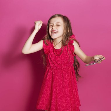 Küçük 8 yaşında kız elleri pembe tarafsız arka plan üzerinde bazı duygusal jest yapmak. O uzun esmer saç ve giyim kırmızı yazlık elbise vardır. Yüzünde komik ifade