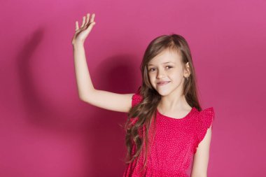 Küçük 8 yaşında kız elleri pembe tarafsız arka plan üzerinde bazı duygusal jest yapmak. O uzun esmer saç ve giyim kırmızı yazlık elbise vardır. Yüzünde komik ifade