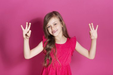 Küçük 8 yaşında kız elleri pembe tarafsız arka plan üzerinde bazı duygusal jest yapmak. O uzun esmer saç ve giyim kırmızı yazlık elbise vardır. Yüzünde komik ifade