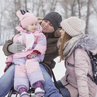 Anne-baba-kız oyun oynayıp kış karlı parkında eğlenen mutlu beyaz aile.