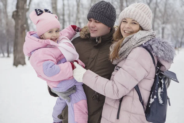Anne-baba-kız oyun oynayıp kış karlı parkında eğlenen mutlu beyaz aile.