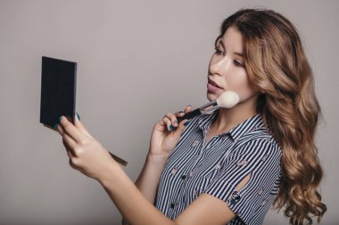 Aynaya bakmak esmer kadın kendini bir akşam tarihi veya düğün, hazırlık için makyaj uygulanması. Nötr arka plan. Kusursuz doğal cilt