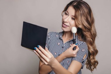 Aynaya bakmak esmer kadın kendini bir akşam tarihi veya düğün, hazırlık için makyaj uygulanması. Nötr arka plan. Kusursuz doğal cilt