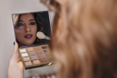 Aynaya bakmak esmer kadın kendini bir akşam tarihi veya düğün, hazırlık için makyaj uygulanması. Nötr arka plan. Kusursuz doğal cilt