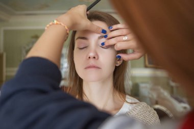 Esmer makyaj sanatçısı kadın beyaz bir esmer gelin, onu düğün photosession veya bir tarih için hazırlama için makyaj uygulanması