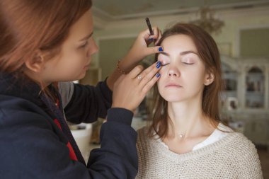 Esmer makyaj sanatçısı kadın beyaz bir esmer gelin, onu düğün photosession veya bir tarih için hazırlama için makyaj uygulanması